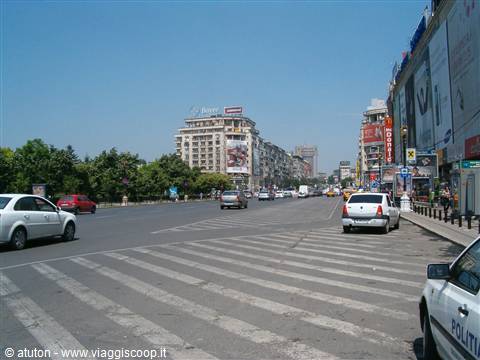 Busy crossing on a wide boulevard with billboards, cars and buildings under blue sky, Bucharest