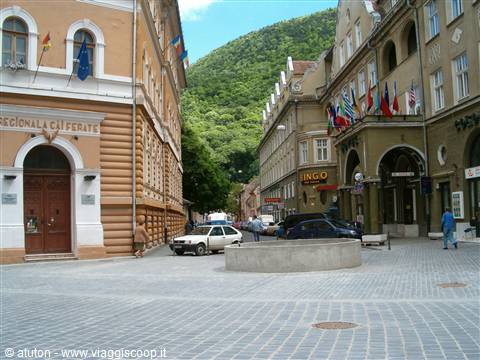 Cobbled square in Brașov with colorful buildings, flags and green hill