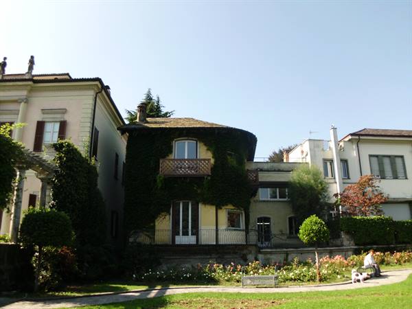 Ivy-covered villa with flower garden, person sitting on bench in sunshine