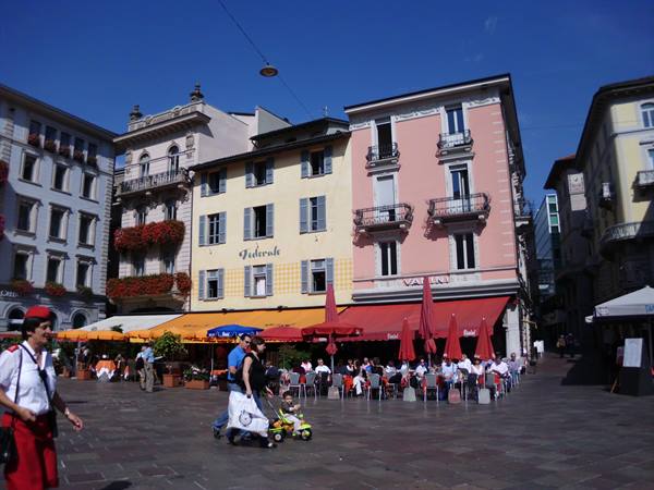 Piazza Riforma in Lugano, cafes with red umbrellas beneath colorful buildings