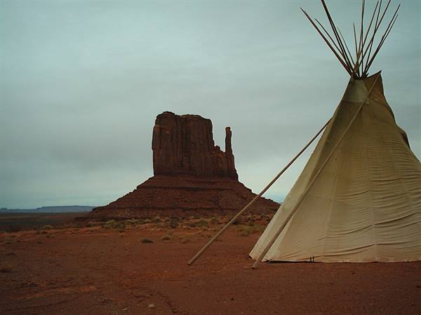 Canvas teepee before Monument Valley's red buttes under gray sky