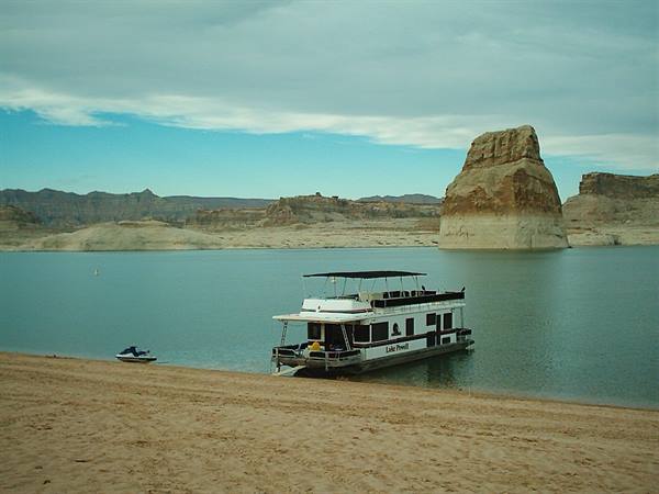 Houseboat beached on the sand at Lake Powell, sandstone butte and cloudy sky