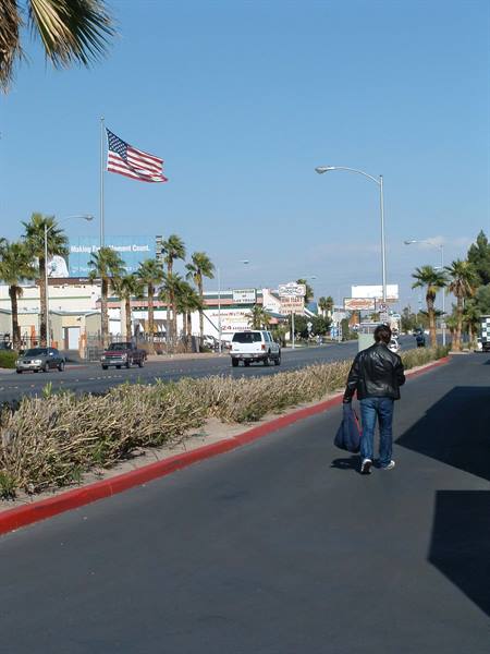 Man in leather jacket walks along Las Vegas Strip past palms and American flag