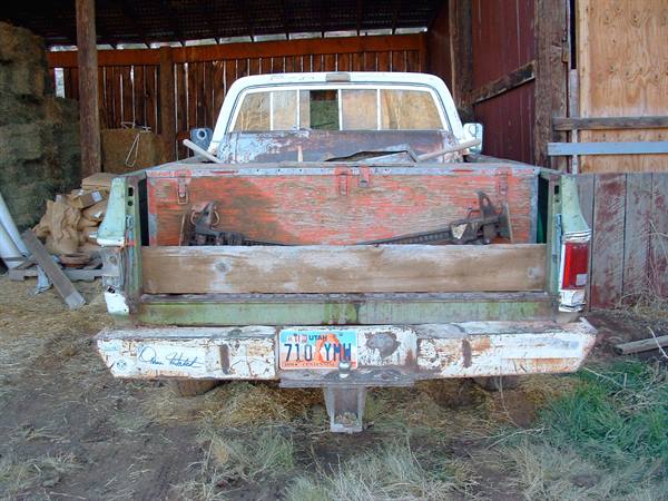 Rusty pickup truck with red wooden bed, parked in front of a barn