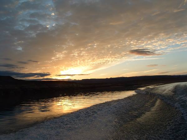 Boat wake gliding over golden water beneath dark hills and evening clouds