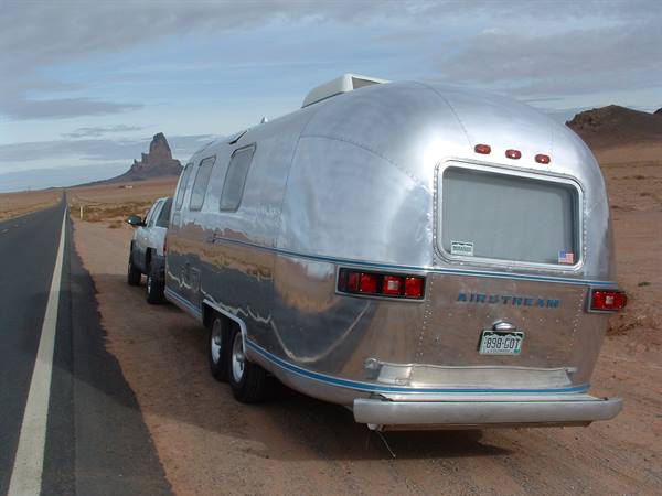 Silver Airstream trailer towed by an SUV along a desert road