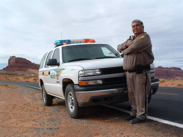 Navajo police officer in uniform standing by his patrol truck in Monument Valley