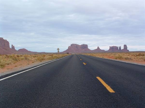 Asphalt road with yellow lines leading to Monument Valley red mesas