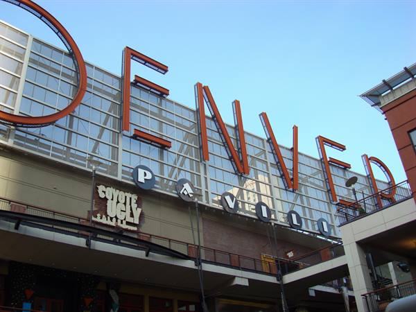 Orange metal Denver Pavilion sign on glass facade, blue sky above