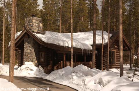 Log cabin with stone chimney, snowy roof and icicles among pines