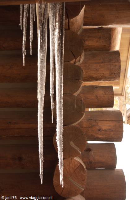 Clear icicles hang from the log roof of a wooden cabin
