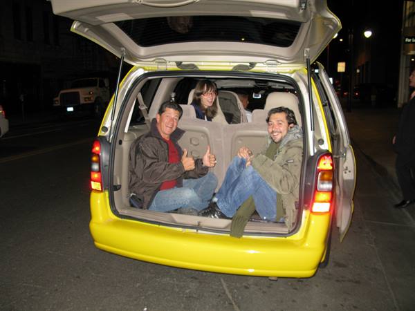 Four friends sitting in the open trunk of a yellow van, city street at night