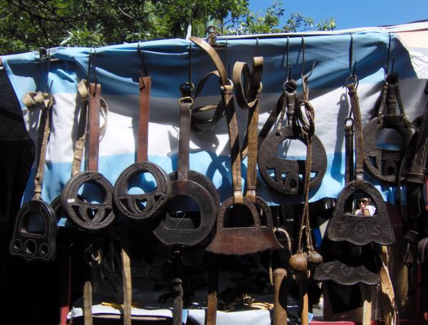 Leather saddles hanging under a blue tarp at market, sunlight