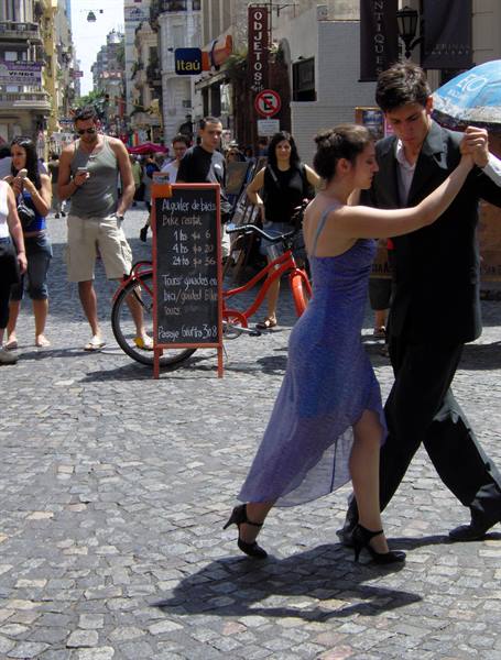 Couple dances tango on San Telmo cobblestone street among pedestrians