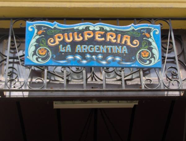 Hand-painted blue sign 'Pulpería La Argentina' above a wrought iron railing