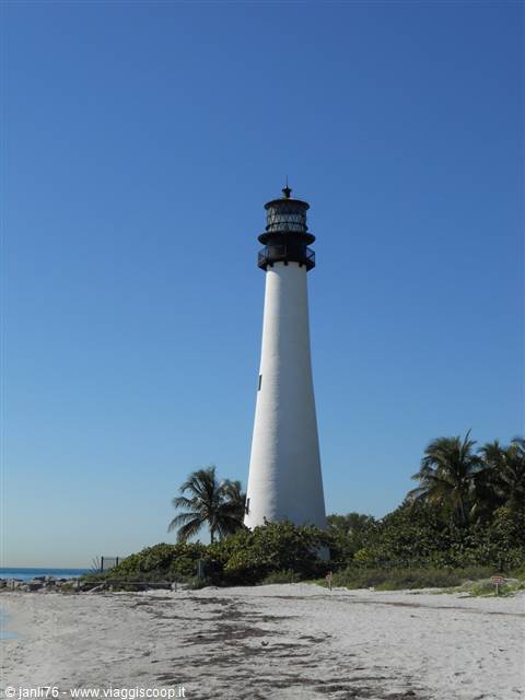 Cape Florida white lighthouse on sandy beach with palm trees and blue sky
