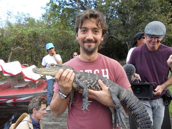 Smiling tourist holds a small alligator, Everglades airboat behind him