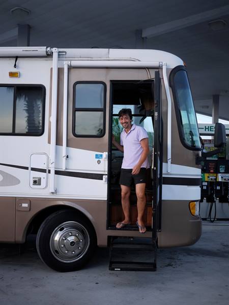 Smiling man in lilac polo on motorhome steps at the fuel pump
