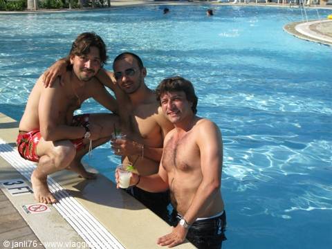 Three friends in swimwear by the pool holding cocktails