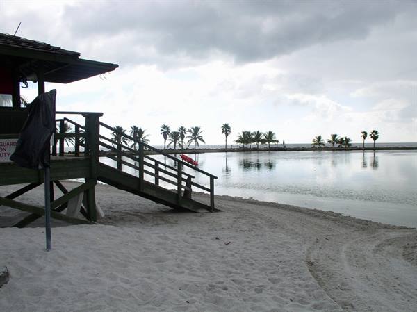 Wooden lifeguard tower on white sand beach, palm trees reflected in calm water