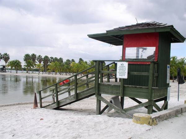 Green and red wooden lifeguard tower on the sand, palm trees behind