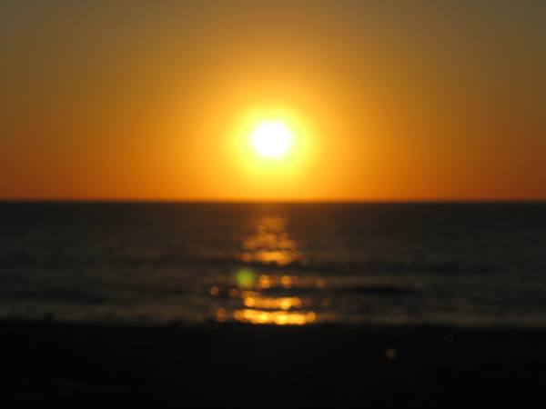 Low sun reflecting on the ocean, dark beach silhouette in backlight