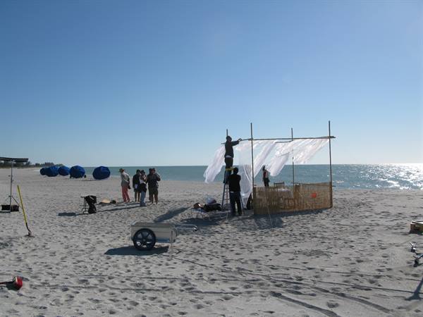 Crew setting up bamboo cabana with white fabric on sandy beach