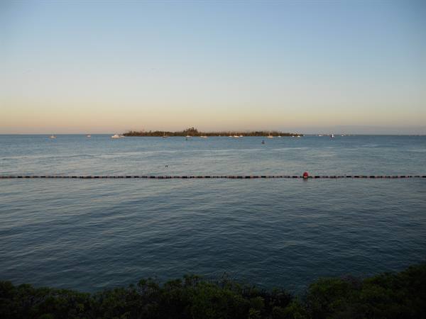 Green island offshore with boats and red buoy on calm dusk sea