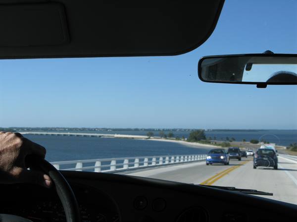Hand on the wheel crossing a long bridge over blue water