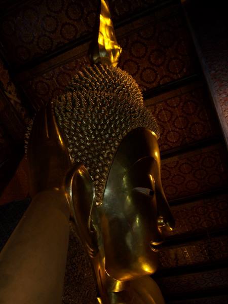 Golden head of the reclining Buddha at Wat Pho temple, warm light