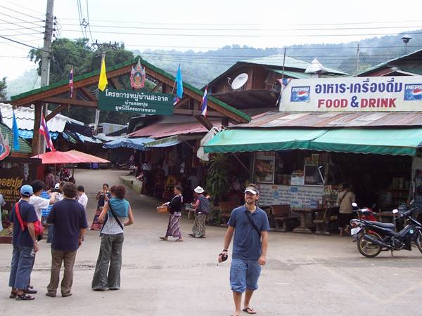 Tourists walk past the market entrance in Mae Hong Son among food stalls and signs