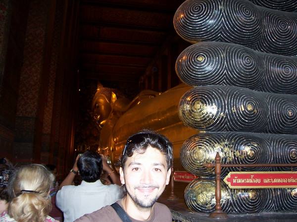 Smiling man in front of the golden Reclining Buddha at Wat Pho, spiral-decorated feet