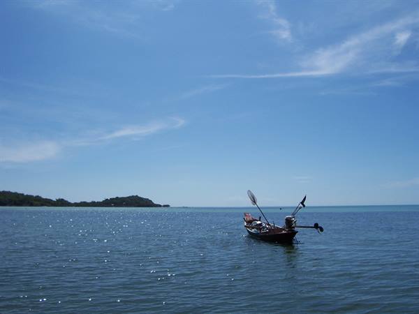 Fishing boat with motor anchored on calm sea, green island in background