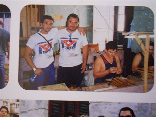 Two young men in white shirts hugging inside a cigar factory