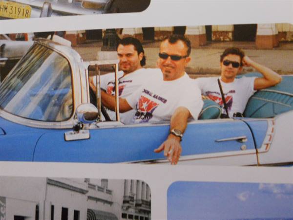 Three friends in white t-shirts riding a vintage blue convertible on a sunny street