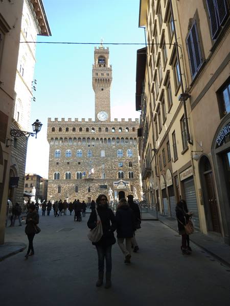 Tourists walking toward Palazzo Vecchio in Florence, crenellated tower with clock