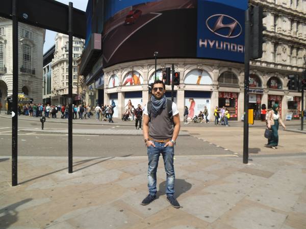 Tourist in jeans and scarf standing before Piccadilly Circus billboards, London