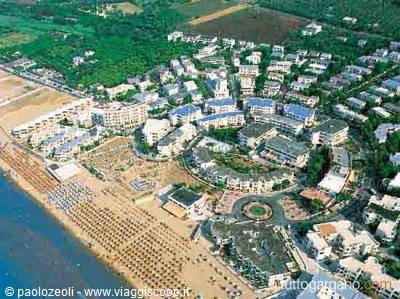 Aerial view of seaside resort with white hotels, beach umbrellas and green pine trees