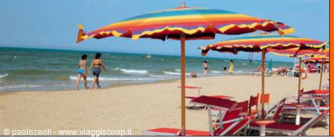 Rainbow beach umbrellas and red sun loungers, vacationers walking on wet sand