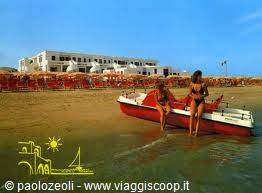 Two girls in bikinis boarding a red boat by the shore, hotel behind