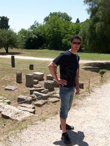 Tourist among ancient stone column ruins at Olympia, Greece, sunny day
