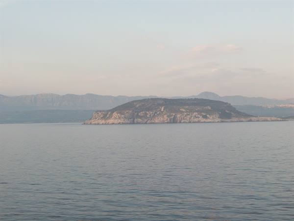 Rocky island in calm sea, hazy hills along the coast