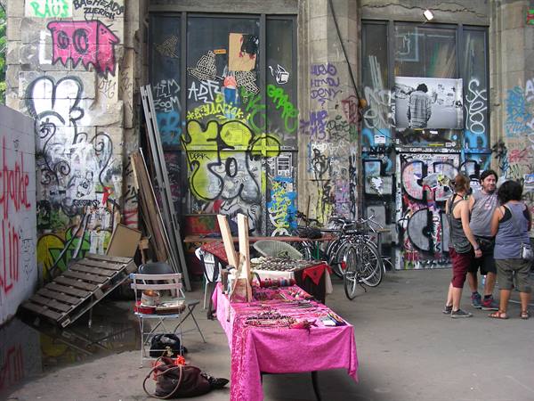Flea market with pink tablecloth before graffiti-covered walls, bicycles and people at Tacheles, Berlin