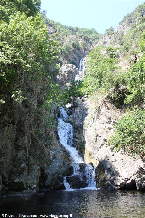 Waterfall cascading over granite rocks among green trees, dark pool below
