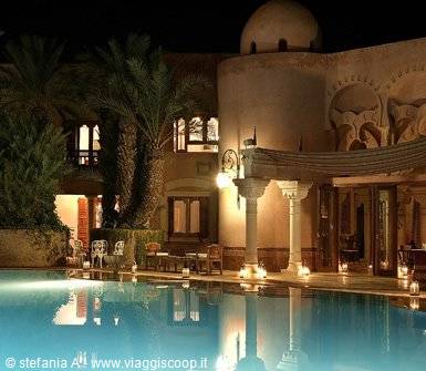 Illuminated pool at night in front of an Arabian-style resort with dome and palms