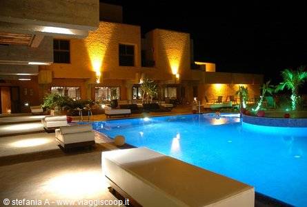 Illuminated pool at night in front of ochre masonry hotel with palms