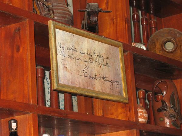 Framed handwritten Hemingway quote on wooden shelf with bottles