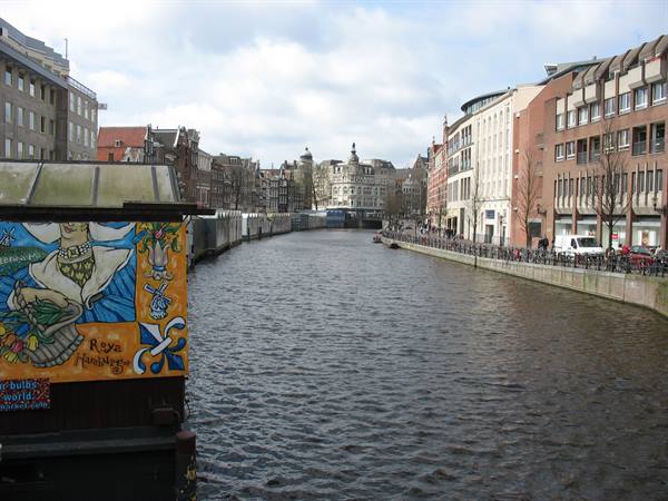 Amsterdam canal with brick buildings, a colorful painted stall and cloudy light