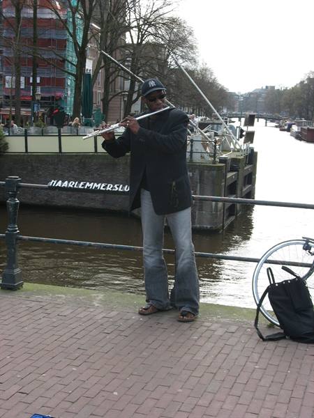 Flutist playing beside Haarlemmersluis canal in Amsterdam, gray skies and a parked bicycle