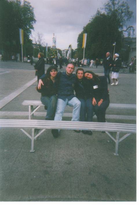Four friends sitting on a metal bench in a square with yellow flags